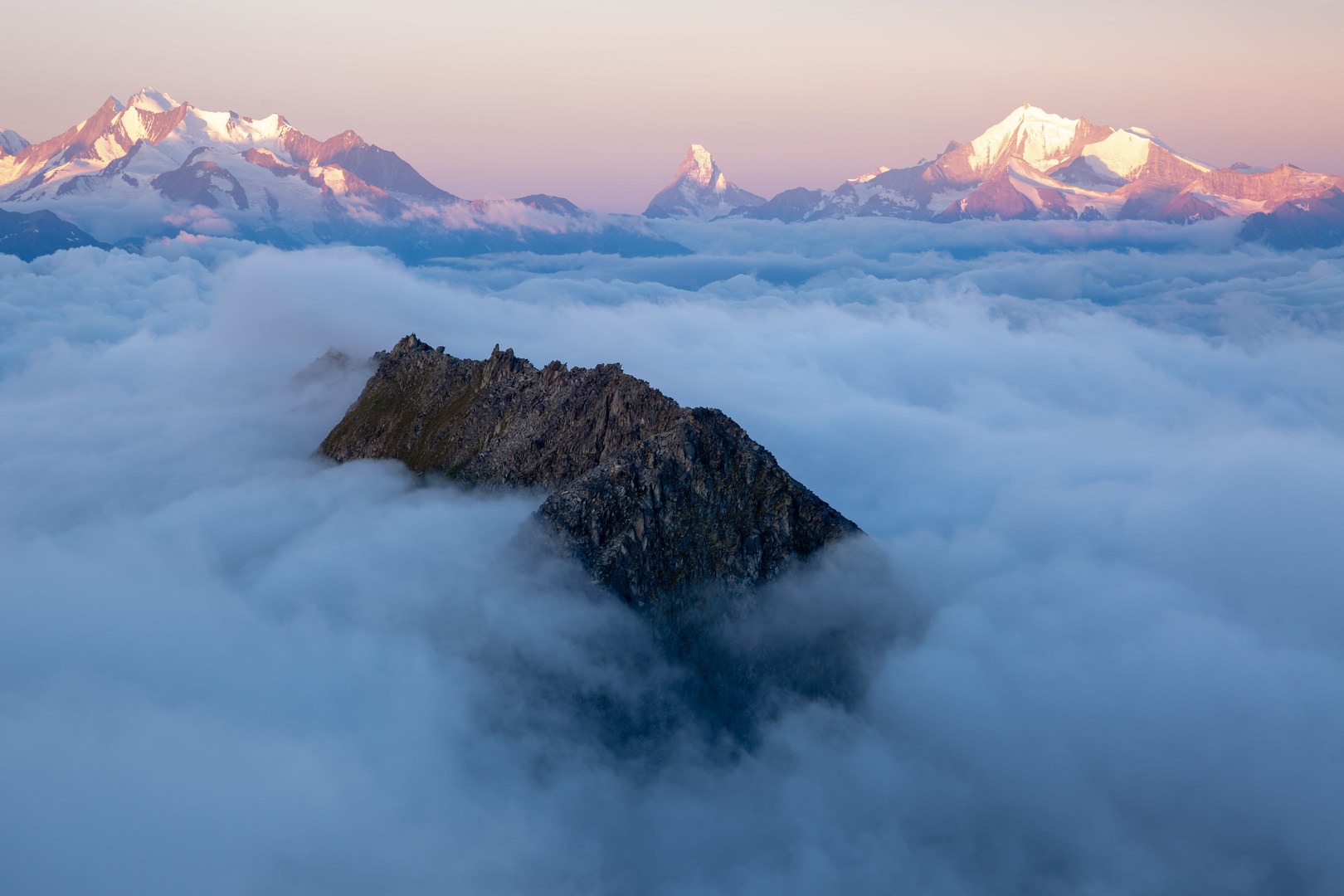 Bettmeralp pokes out of the clouds in the foregroud with the Matterhorn, the Dufourspitze, and Dent Blanche in the distance.