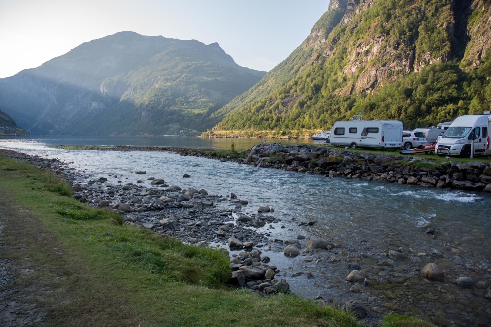 A river separates two parts of the campground with view of fjord.