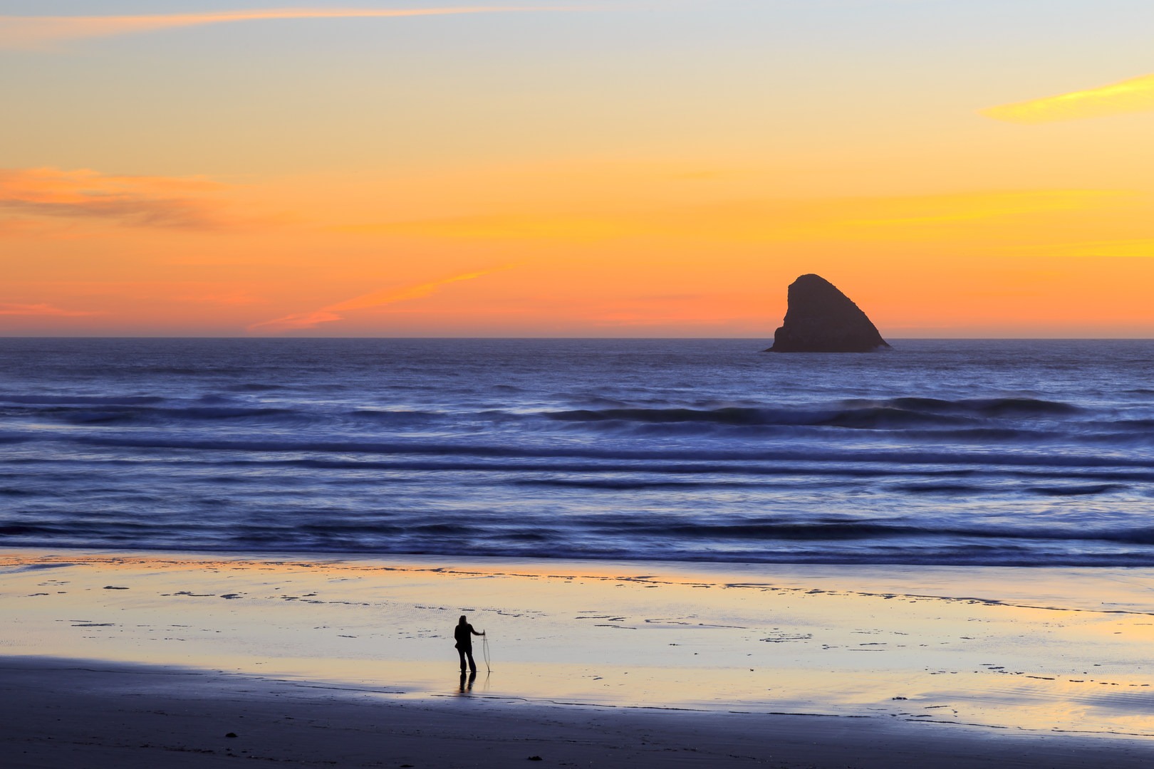 A beach walker enjoys the sunset with Pyramid Rock off-shore.